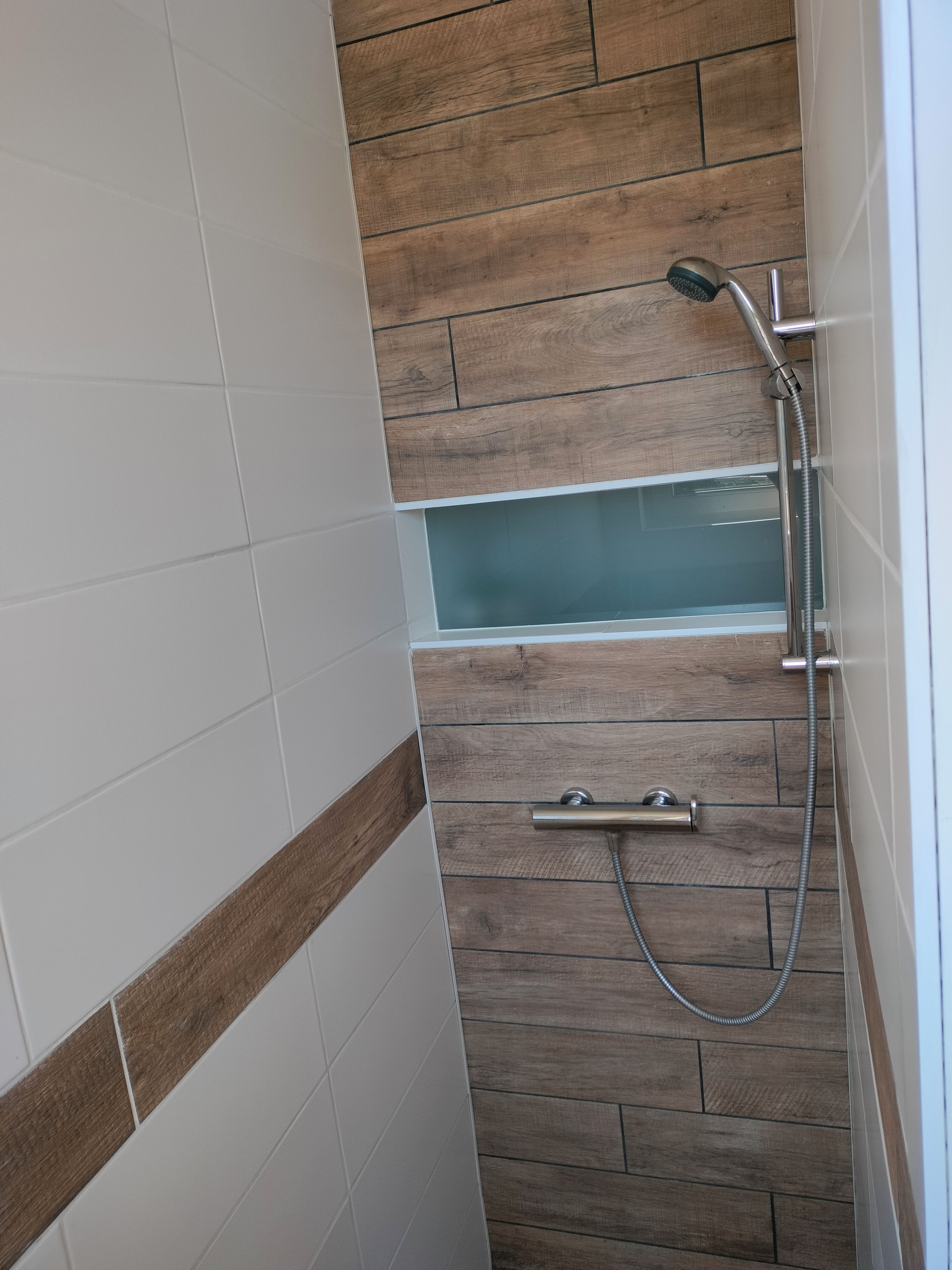 Un espace douche avec un mur recouvert de panneaux en bois, une baignoire entourée de parois en verre et une douchette à main.