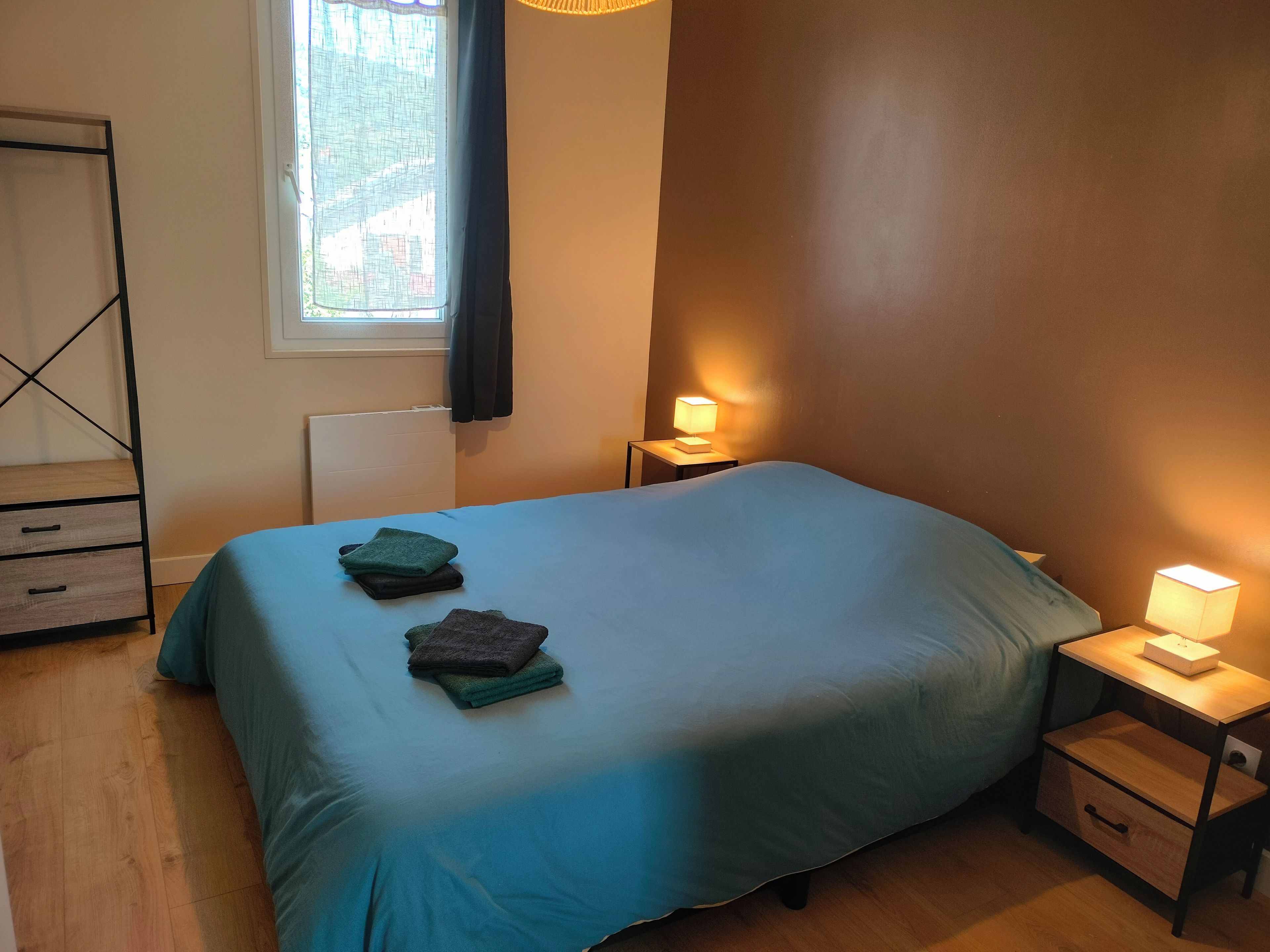Ein Schlafzimmer mit einem Bett, zwei Nachttischen, einem Fenster mit Vorhängen und einer Heizung.