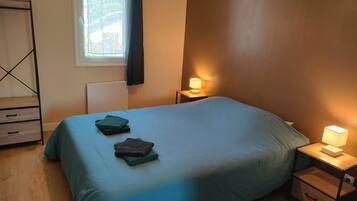 Ein Schlafzimmer mit einem Bett, zwei Nachttischen, einem Fenster mit Vorhängen und einer Heizung.