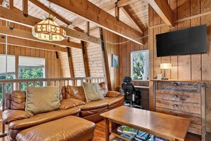 A wooden interior with a leather sofa, a television, and a desk with drawers. - Hot Tub + Firepit + Grill | Mountain Views + Mins to Slopes | Bear Pine Lodge (Big Bear)