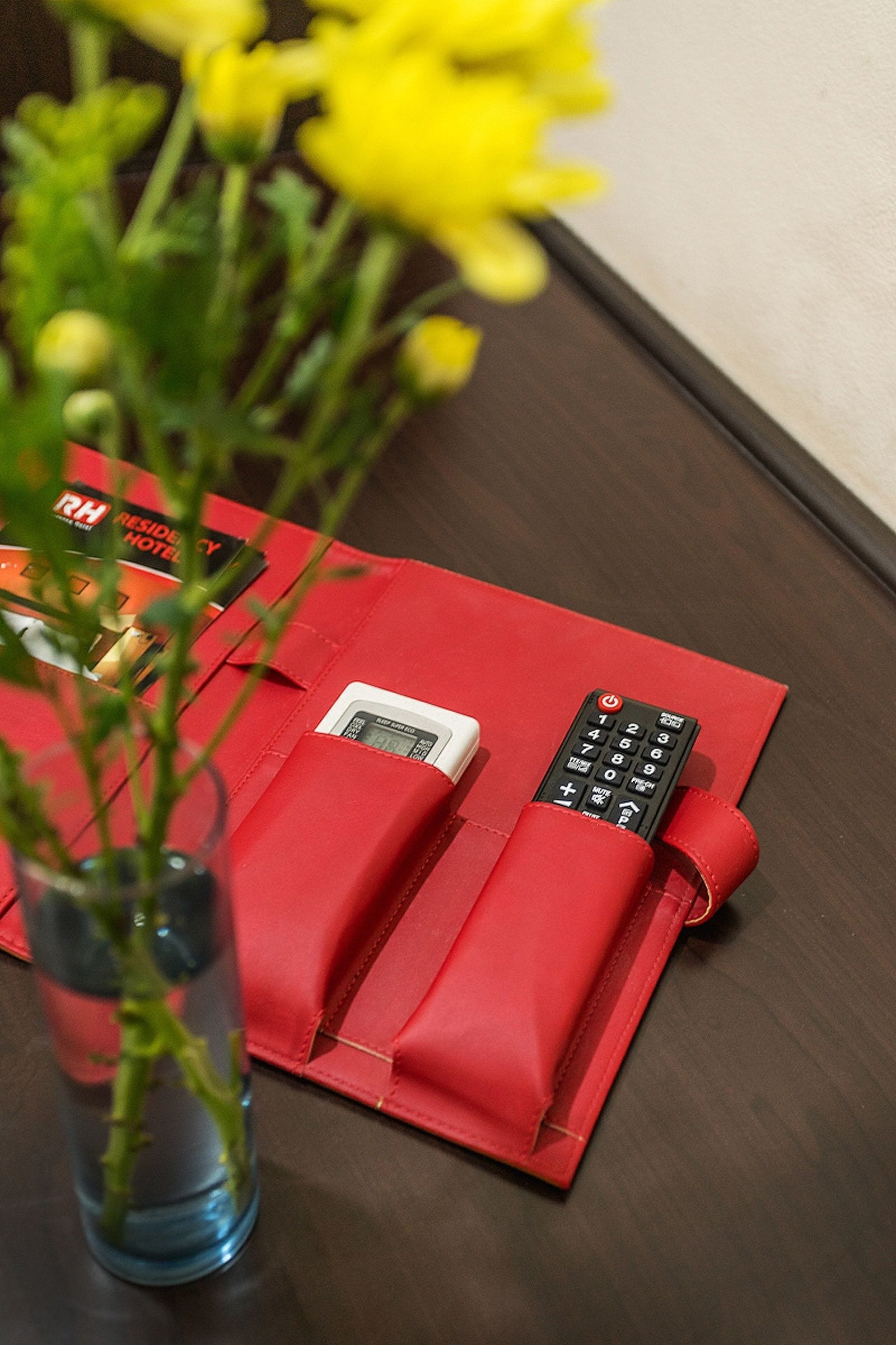 Un sobre rojo con un control remoto y un reloj digital sobre una mesa de madera.