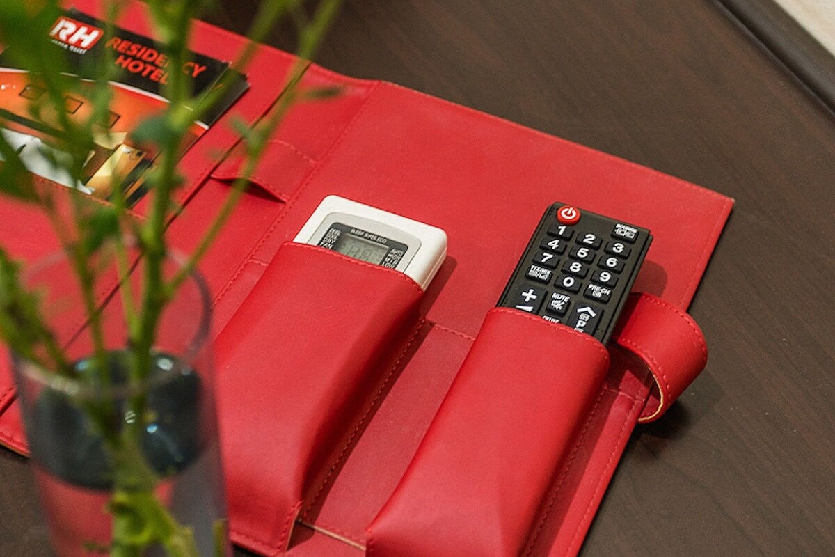 Une enveloppe rouge contenant une télécommande et une horloge numérique, posées sur une table en bois.