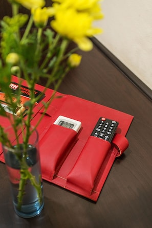 A red envelope with a remote control and a digital clock on a wooden table. - SHRI VRINDAVAN (Bangkok)