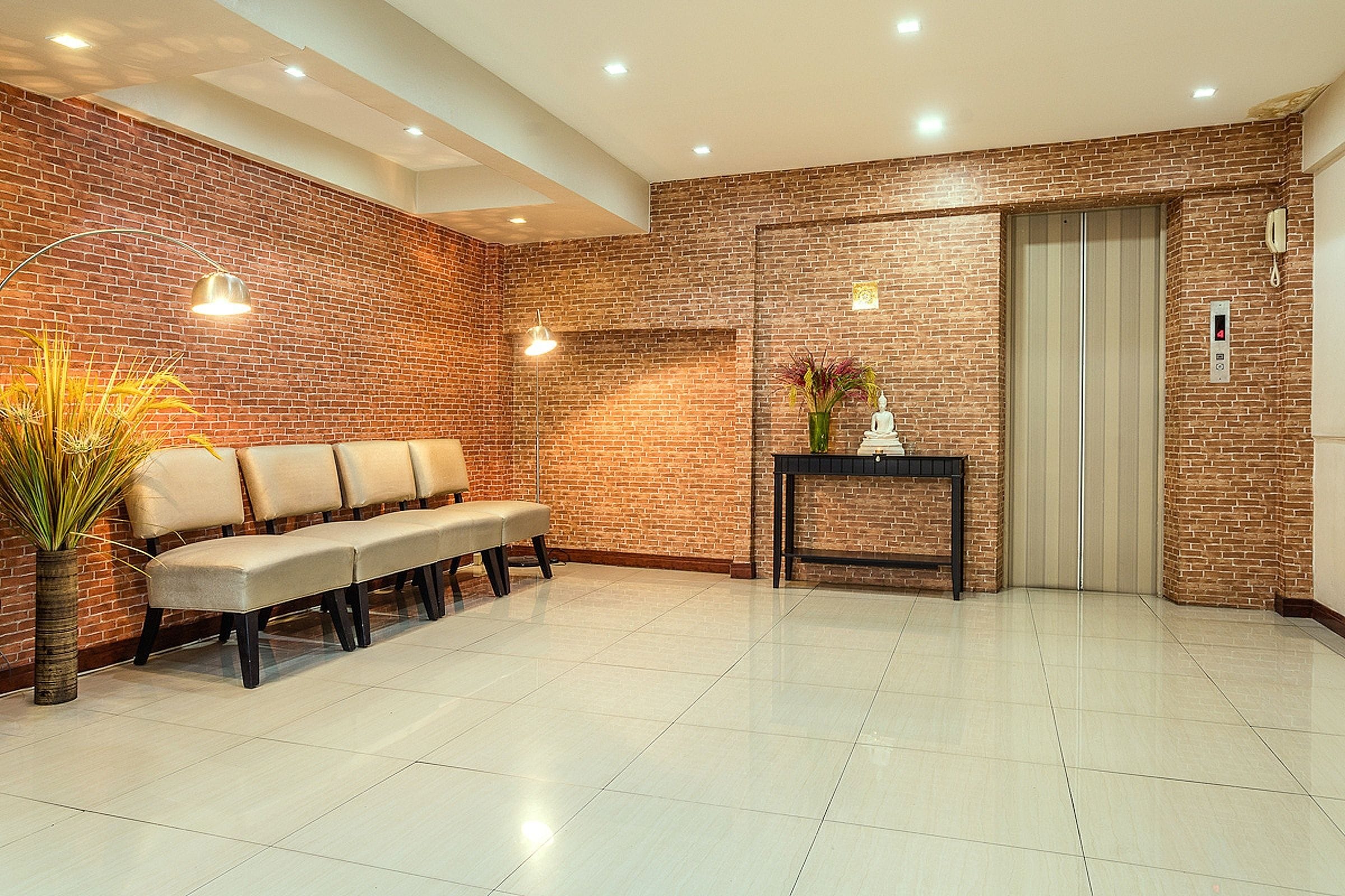 A reception area with a brick wall, a bench, a vase with flowers, a small table, and an elevator.