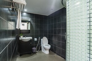 Une salle de bain moderne avec des toilettes blanches, des murs recouverts de carreaux foncés, un lavabo avec un miroir au-dessus et un porte-serviettes avec des serviettes.