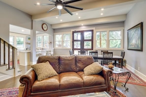 A spacious living room with a brown leather sofa, a dining area with a wooden table and chairs, and large windows allowing natural light. - Quiet Countryside Escape w/ Views in Talking Rock (Talking Rock)