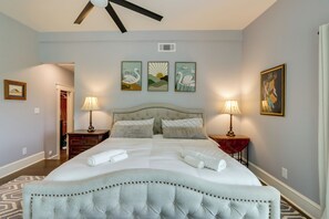Ein Hotelzimmer mit einem großen Bett, zwei Nachttischen mit Lampen, einem Deckenventilator und drei an der Wand befestigten Kunstwerken.