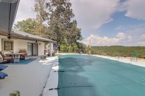 Ein überdachter Außenbereich mit Pool, Sitzgelegenheiten und Blick auf Bäume und Hügel.