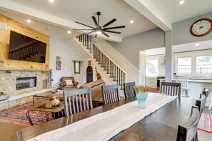 A spacious living room with a fireplace, a dining area with a long table, and a staircase leading to an upper level. - Quiet Countryside Escape w/ Views in Talking Rock (Talking Rock)