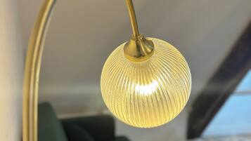 Een kamer met een groene bank, een gebogen metalen vloerlamp en uitzicht op een strand door een raam.
