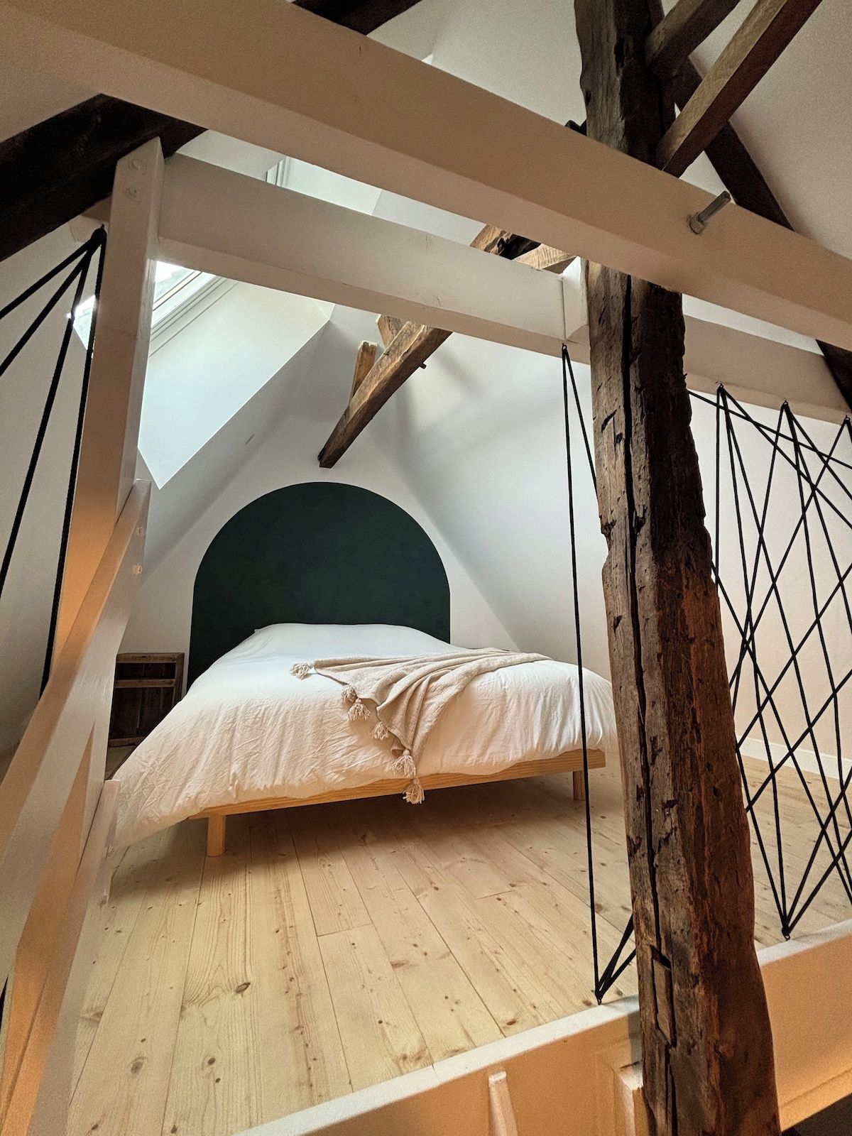 Une chambre à coucher aménagée dans un grenier, avec un plafond en pente, un plancher en bois et un lit doté d’une tête de lit verte.