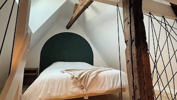 Une chambre à coucher aménagée dans un grenier, avec un plafond en pente, un plancher en bois et un lit doté d’une tête de lit verte.