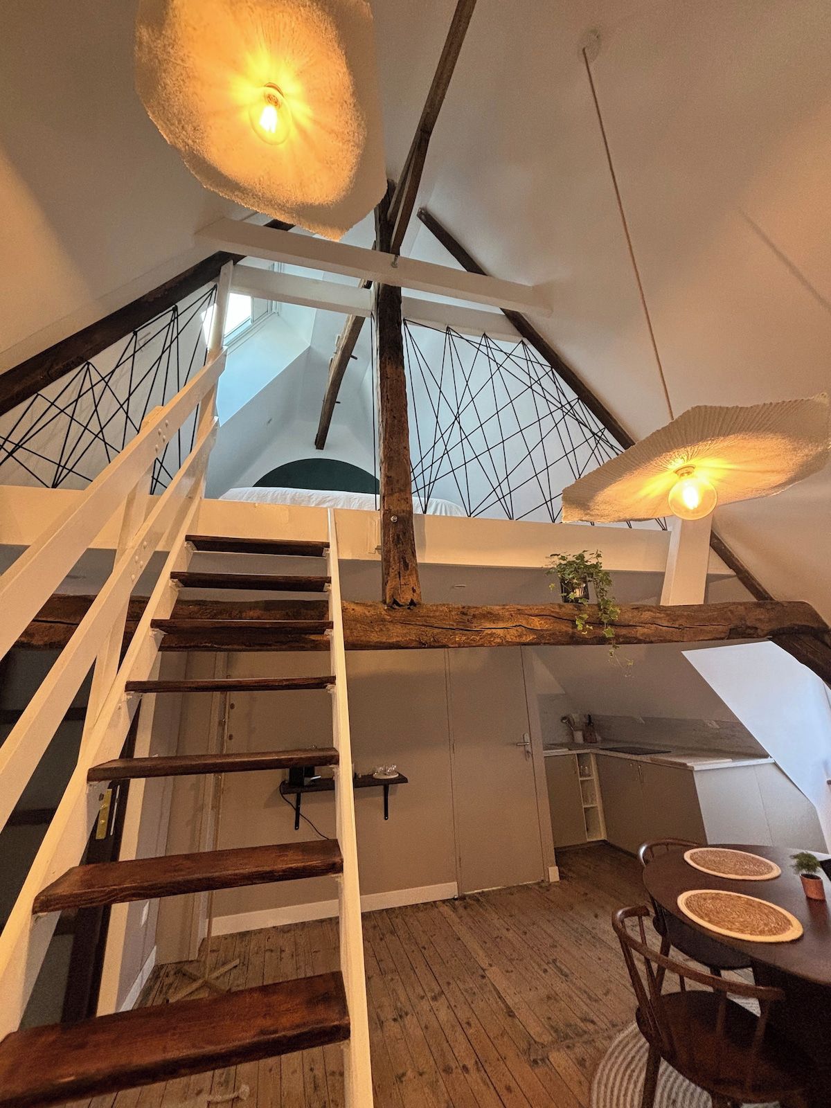 Un intérieur à plusieurs niveaux, doté d’un escalier en bois, d’un coin repas avec une table ronde et offrant une vue sur le ciel grâce à un motif géométrique ornant le plafond.