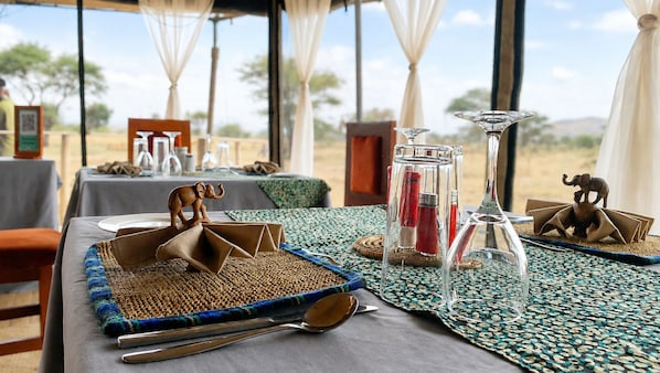 A dining table set with a woven placemat, a wooden elephant centerpiece, clear glass candle holders, and a small elephant figurine.