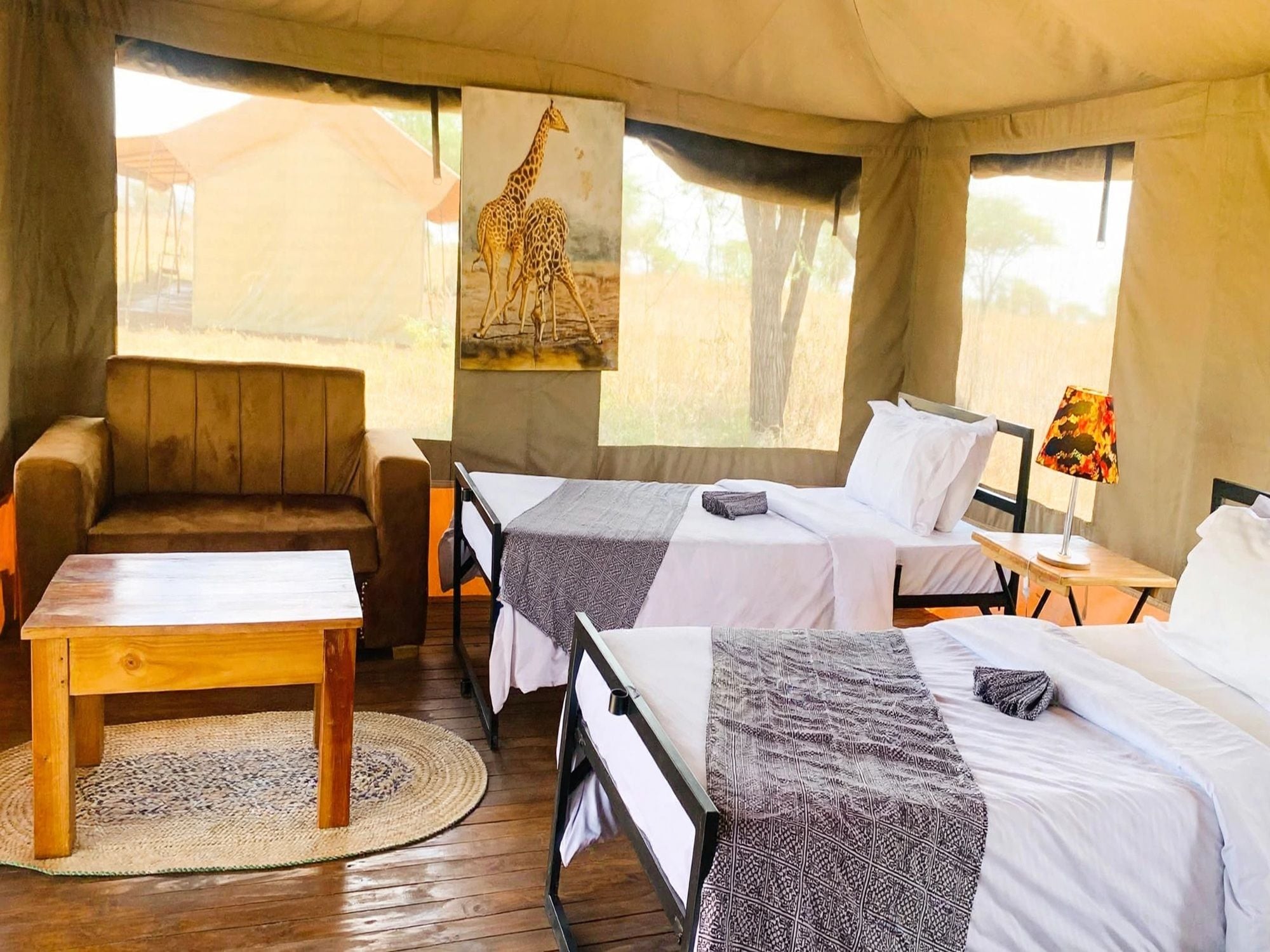 Acomodação em tenda com duas camas, um sofá, uma mesa e uma pintura de girafa.