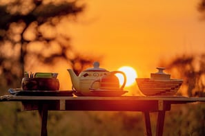 A table with a teapot, cups, and a bowl set against a sunset.