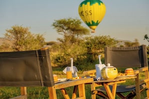 A table set outdoors with camping chairs, a portable stove, a kettle, a mug, and a hot beverage.
