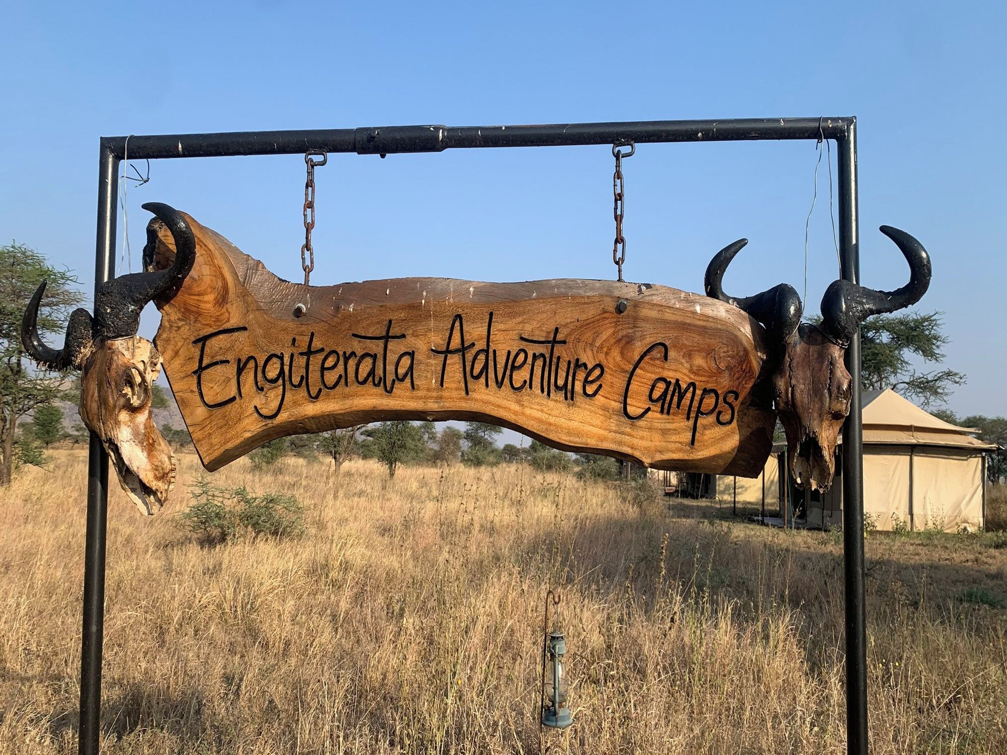Uma placa de madeira com o texto 'Engiterata Adventure Camps' pendurado em uma estrutura de metal.