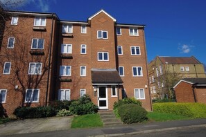 A multi-story brick apartment building with a central entrance, multiple windows, and a small front garden. - Bright 2BDR Apt with Garden View in Greenwich (London)