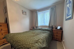 A bedroom with a bed, a dresser, a nightstand, a window with curtains, and a wall-mounted picture. - Bright 2BDR Apt with Garden View in Greenwich (London)
