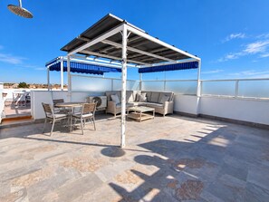 A rooftop terrace with a covered seating area, a table, and chairs. - Jardin del Mar House Torrevieja (Torrevieja)