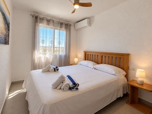 A hotel room with a bed, a ceiling fan, an air conditioning unit, a bedside lamp, and a window with curtains. - Jardin del Mar House Torrevieja (Torrevieja)