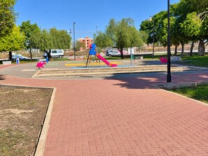 A paved walkway with a playground featuring a slide and swings. - Jardin del Mar House Torrevieja (Torrevieja)