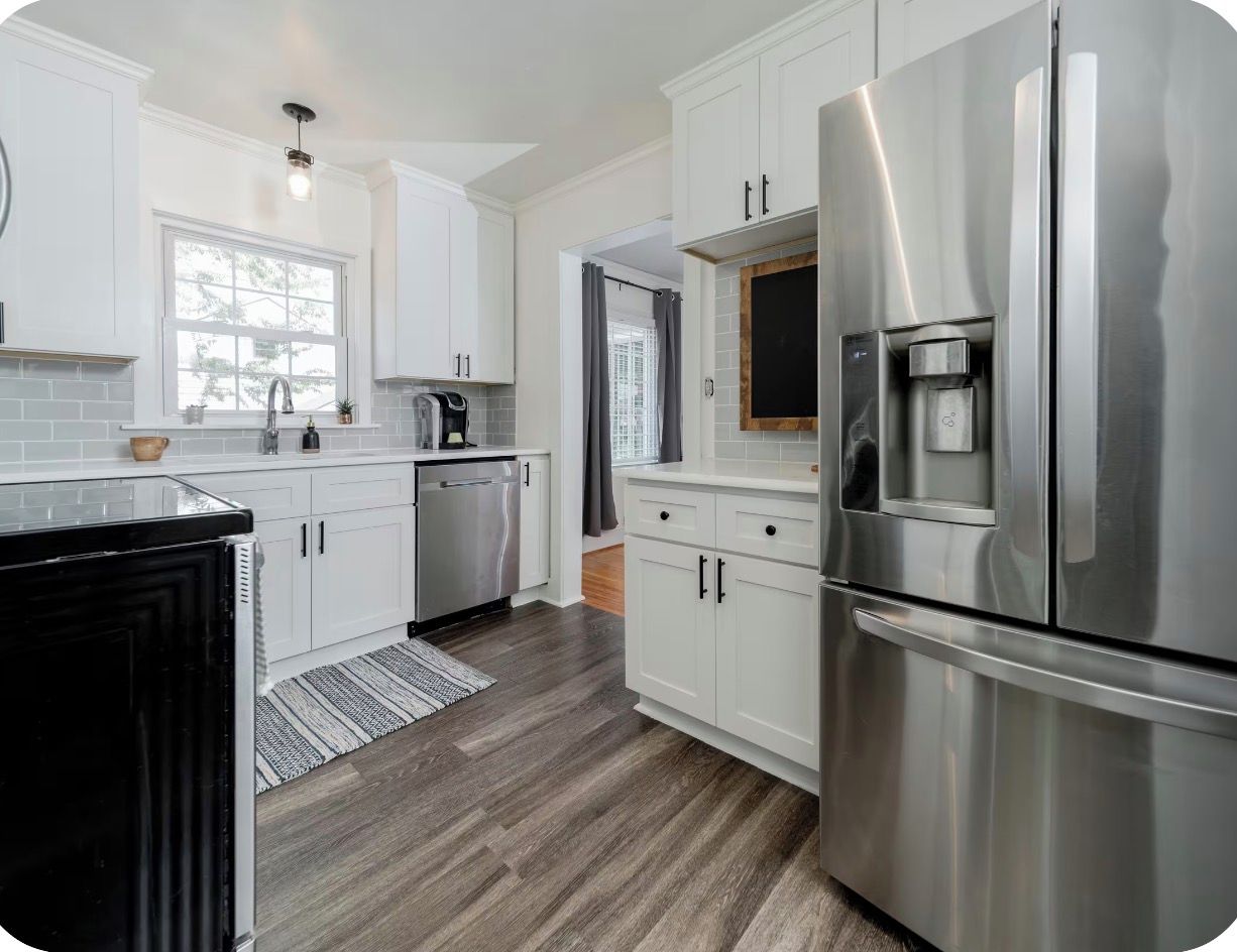 A modern kitchen with white cabinets, stainless steel appliances, and a wooden floor.