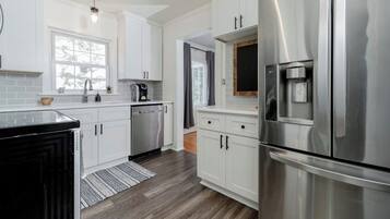 A modern kitchen with white cabinets, stainless steel appliances, and a wooden floor.