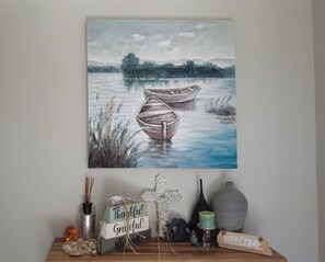 A painting of a calm lake with boats, a wooden sign with 'Thankful Grateful Welcome', and decorative items on a shelf.