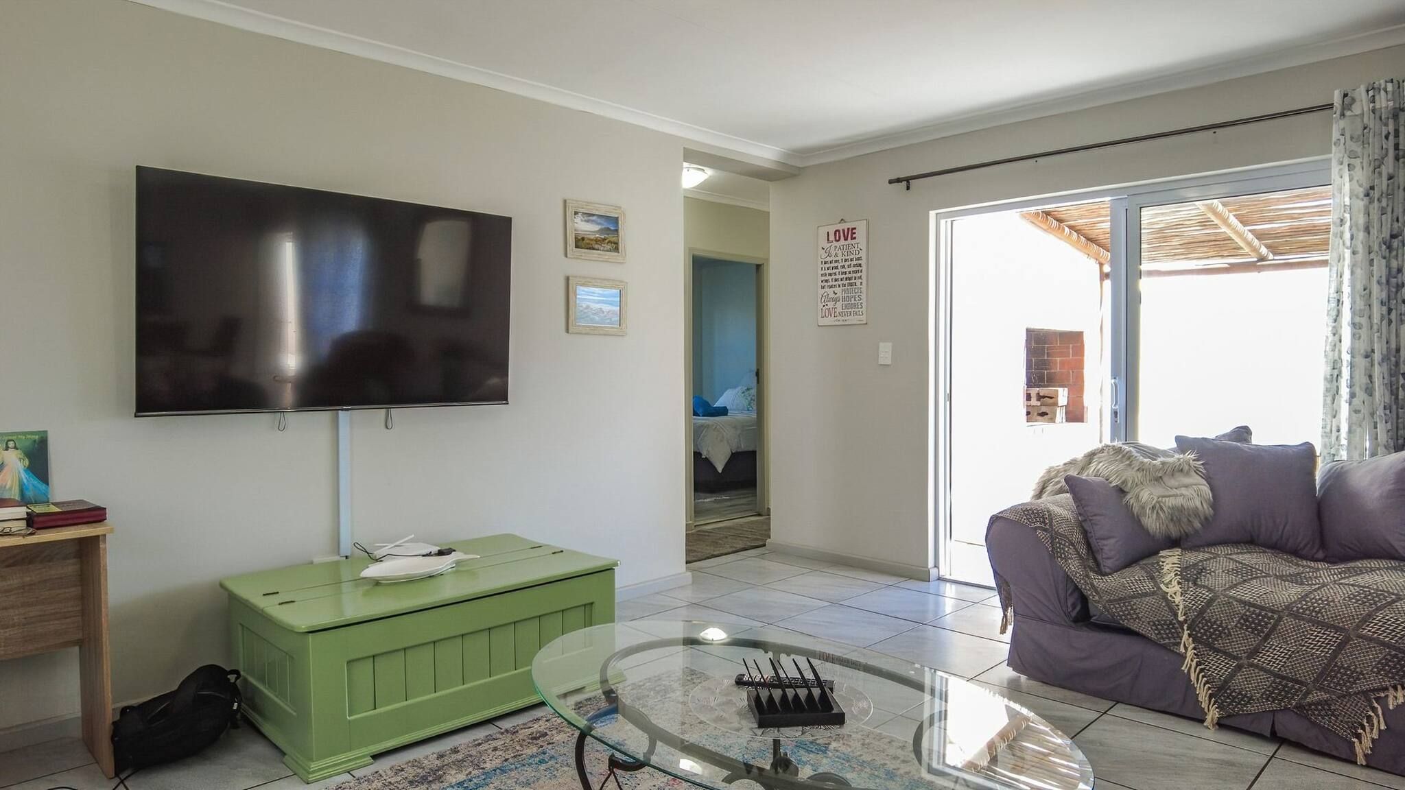 A living room with a flat-screen TV, a green cabinet, a glass coffee table, and a purple sofa.