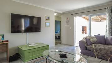 A living room with a flat-screen TV, a green cabinet, a glass coffee table, and a purple sofa.