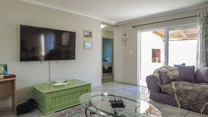 Una sala de estar con un televisor de pantalla plana, un mueble verde, una mesa de centro de vidrio y un sofá morado.