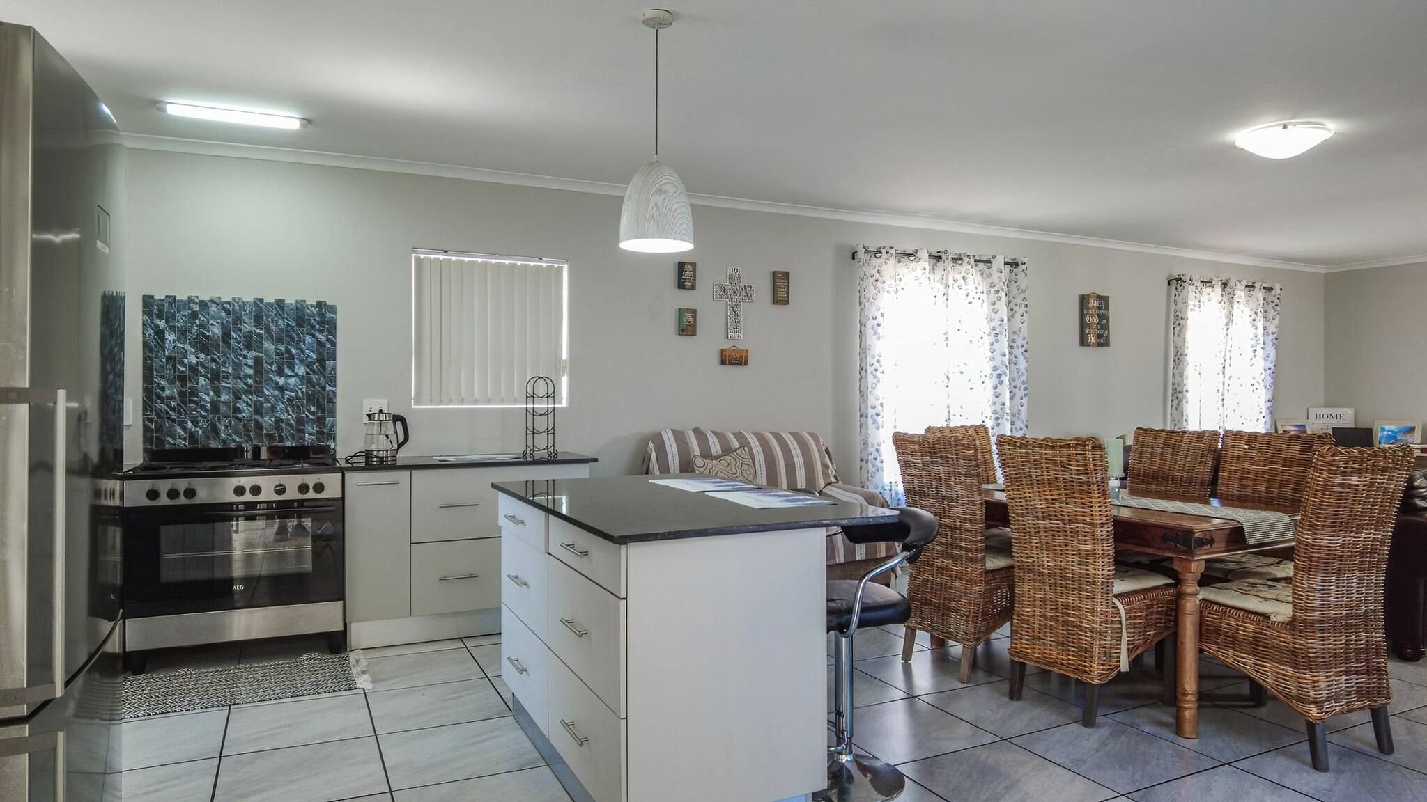 Une cuisine moderne dotée d’une cuisinière intégrée, d’un coin repas avec des chaises en osier et d’un petit îlot central avec un évier.