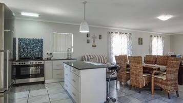 Une cuisine moderne dotée d’une cuisinière intégrée, d’un coin repas avec des chaises en osier et d’un petit îlot central avec un évier.