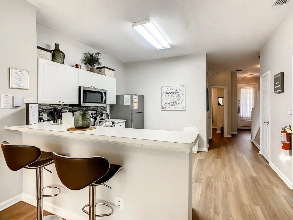 A modern kitchen with white cabinetry, a central island with stools, and a microwave.