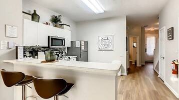 A modern kitchen with white cabinetry, a central island with stools, and a microwave.