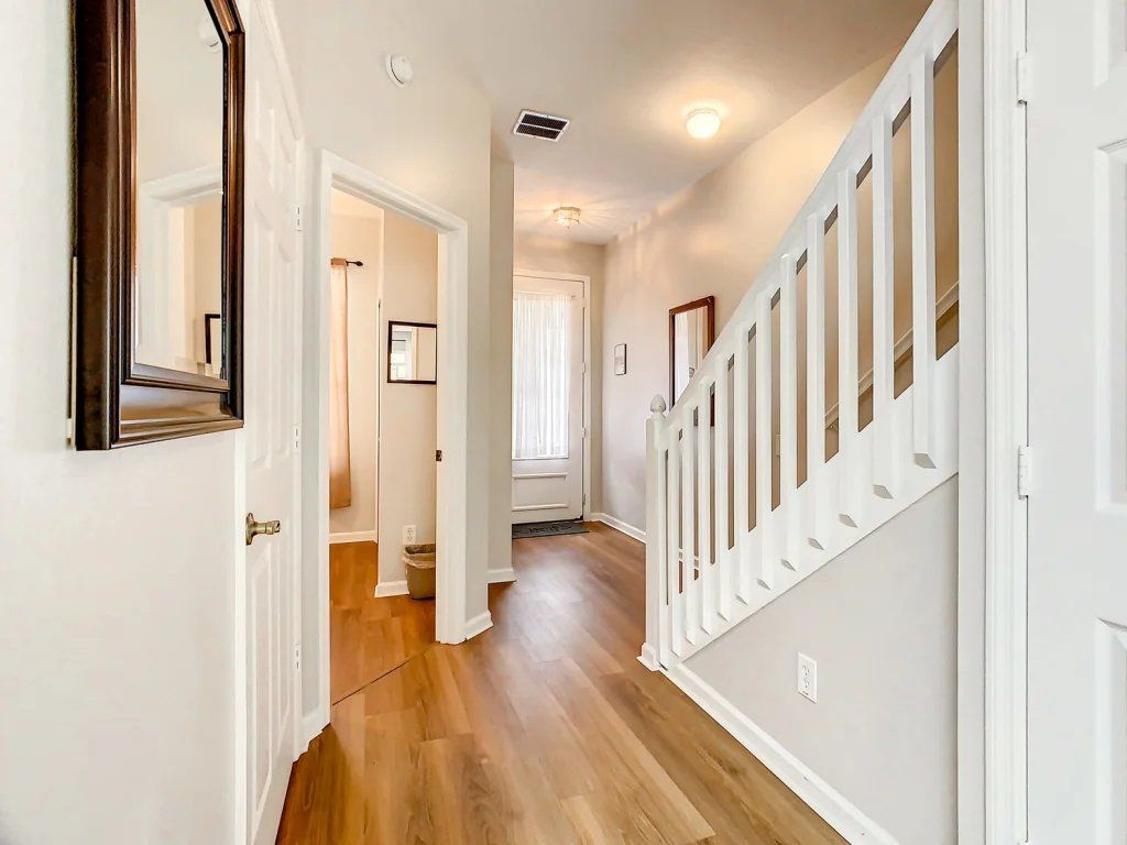 A hallway with a wooden floor, white walls, and a white staircase with a railing.