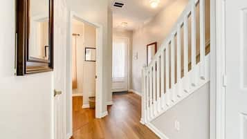 A hallway with a wooden floor, white walls, and a white staircase with a railing.