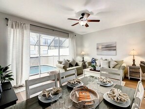 A dining area with a table set for four, a ceiling fan, and a view of a swimming pool through large windows. - Windsor Palms - 35431 (Kissimmee)