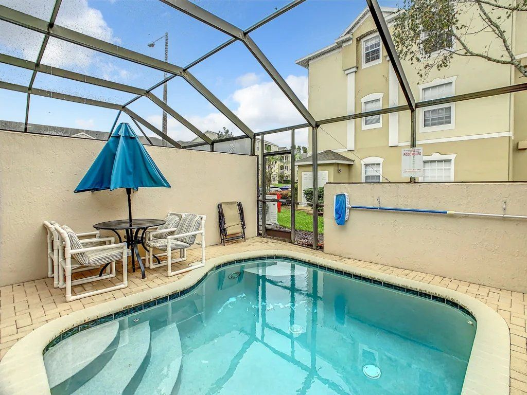 A swimming pool with a glass enclosure, surrounded by a patio area with chairs and a table.