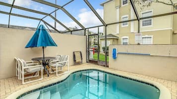 A swimming pool with a glass enclosure, surrounded by a patio area with chairs and a table.