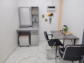 A small, modern room with a grey cabinet, a small table with chairs, a heater, and a wall-mounted air conditioner.