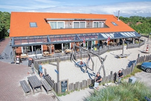 A restaurant with a red tiled roof, outdoor seating, and a wooden fence. - Modernly furnished chalet in the heart of Texel (Den Burg)