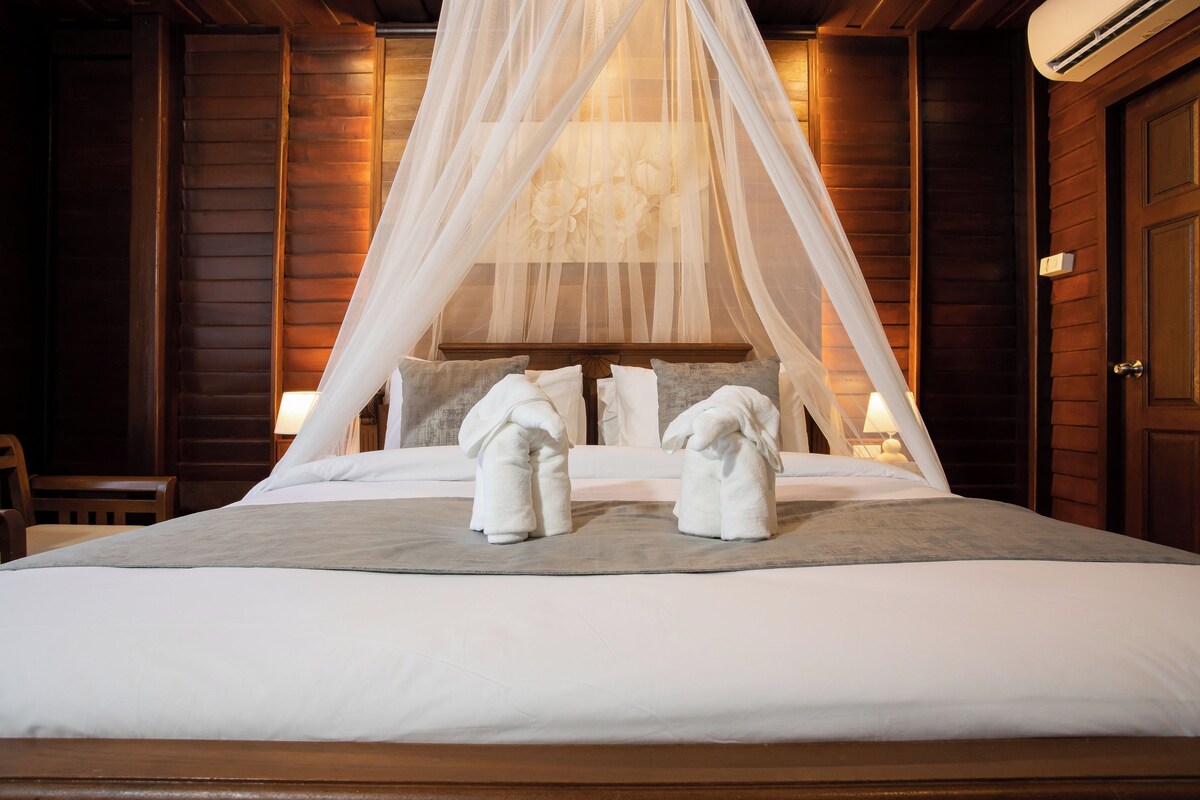 Una cama bien hecha con dosel, dos almohadas y dos toallas.