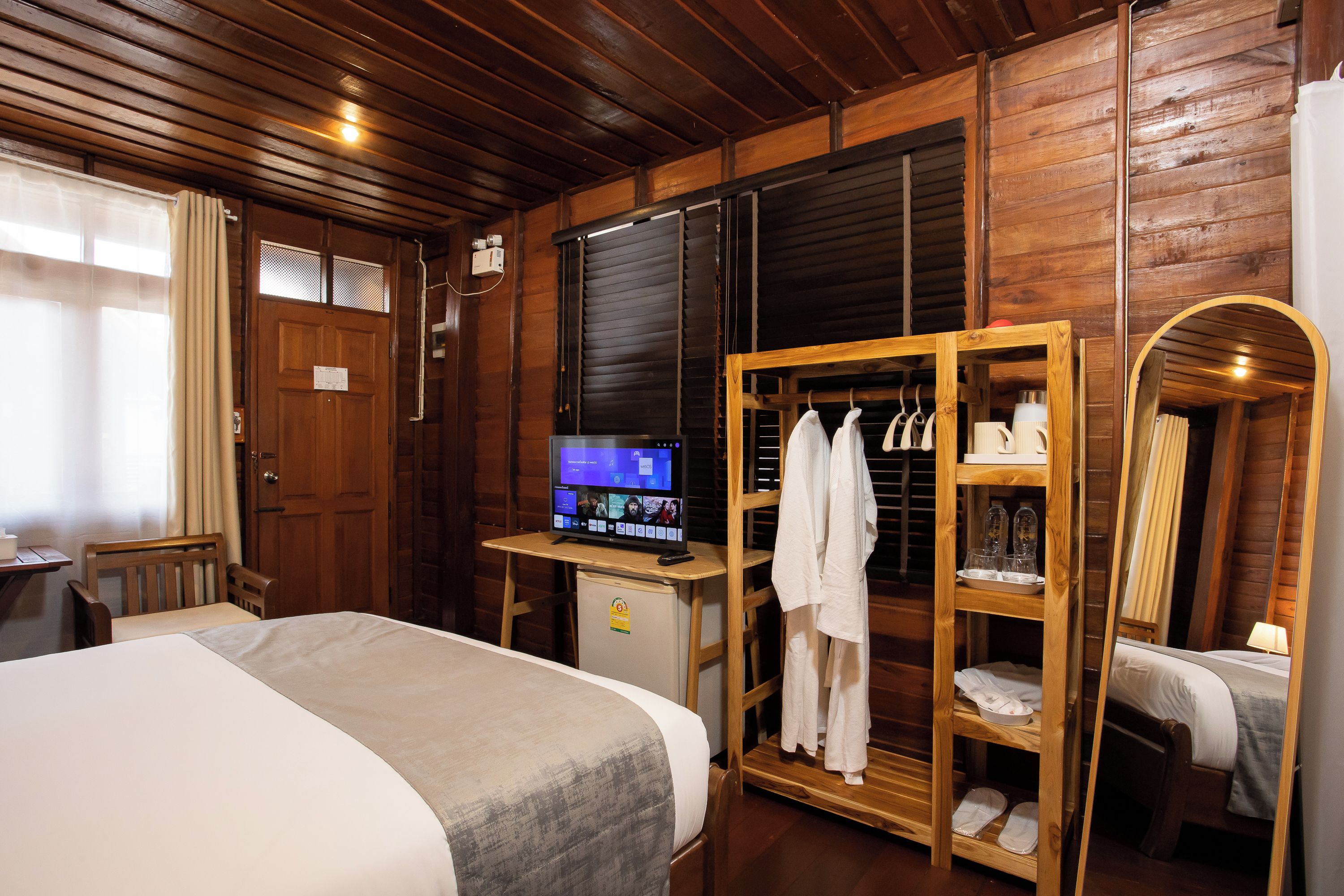 A wooden room with a bed, a desk with a computer, a wardrobe, and a mirror.
