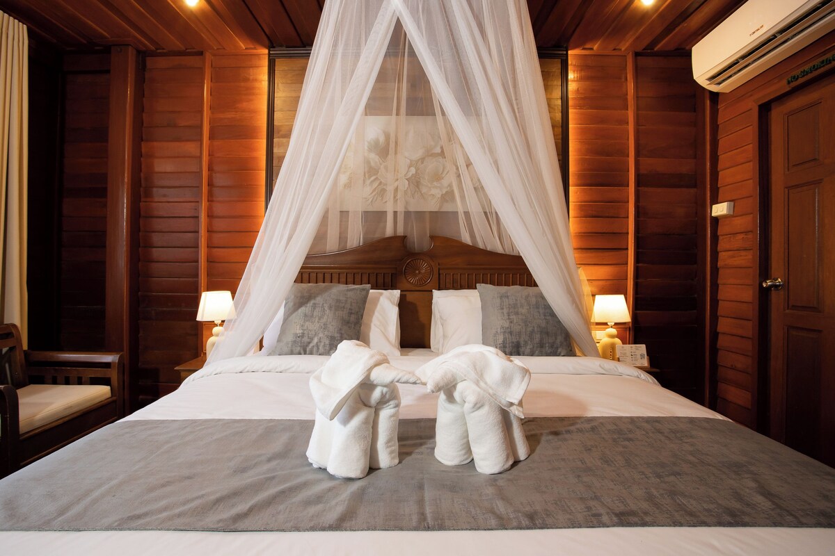 Habitación de hotel con una cama con dosel, dos lámparas de noche y una pared de madera.