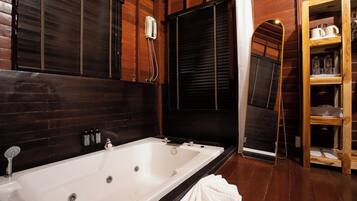 A bathroom with a large bathtub, wooden walls, a mirror, and a shelf with toiletries.