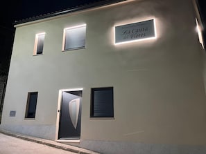 A building with a sign reading 'Alojamiento Turístico La Casita del Flores' and a modern door with a large V-shaped window.