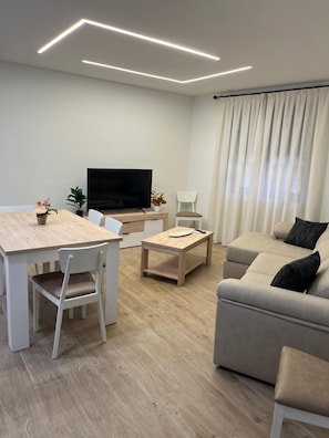A modern living room with a flat-screen TV, a sofa, a dining table, and a coffee table.